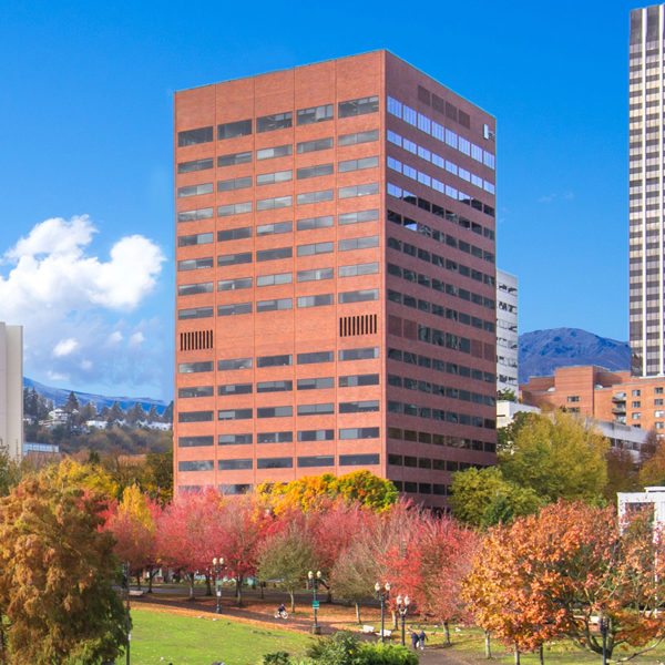 The entire Umpqua Bank Plaza Building and Portland skyline with blue sky and trees.